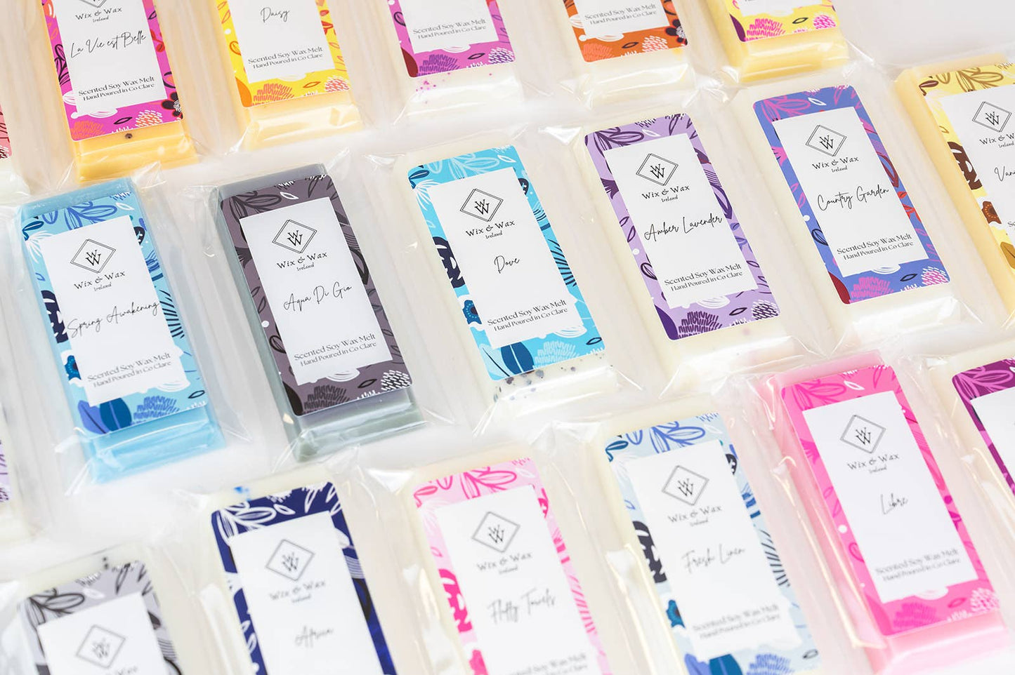 Assorted wax melts with colorful labels arranged in a grid.